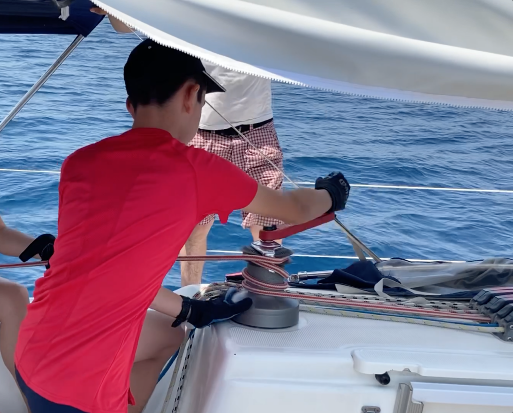 Maniobra de izado y recogida de vela mediante molinete, manivela, cabos y pianos.